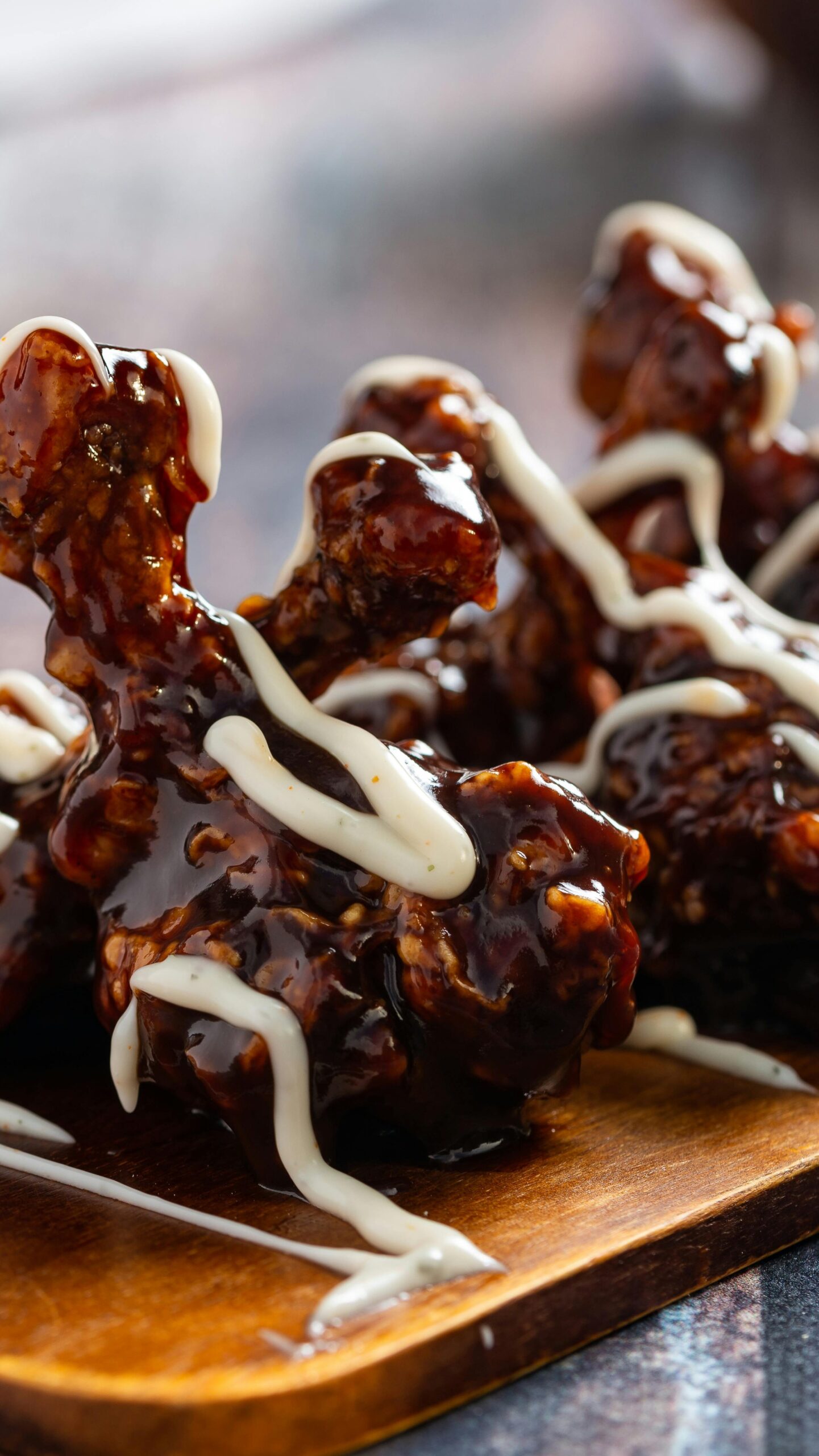 Close-up of glazed chicken wings drizzled with sauce on a wooden board.